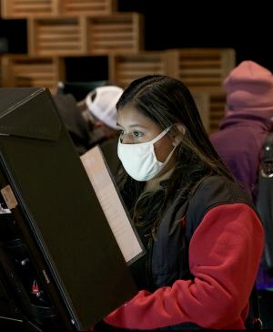 Two women wearing masks use voting machines
