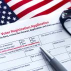 A voter registration form with a pen and glasses on top of an American flag