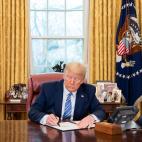 Donald Trump at his desk in the Oval Office signing a document