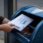 Close up of a woman's hands putting an envelope into a large blue mailbox.