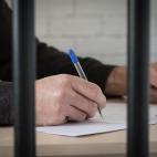 A man's hand holding a pen and writing behind bars