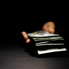 A hand emerges out of the dark holding a stack of $100 bills