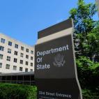 A sign saying "Department of State" in front of a plain concrete building with windows