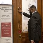 A man stands with his hand against a door. A sign on the doors reads "Governor's Public Reception Room, Closed, Do Not Enter, Meeting in Progress"
