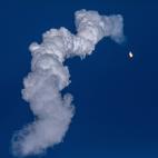 A small light againsta blue sky with a large plume of smoke trailing behind it