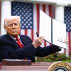 Donald Trump holding up an signed executive order while sitting in front of American flags