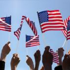 Group of People Waving American Flags over blue sky. Adobe Stock image.