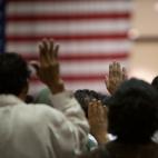 People raise their hands while standing in front of an American flag on the wall
