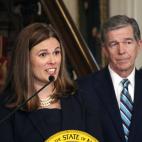 A woman speaking at a podium with a man standing behind her