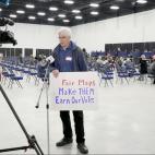A man standing in front of a TV camera holding a sign that says "Fair Maps. Make them earn our vote."