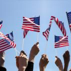 Group of People Waving American Flags over blue sky. Adobe Stock image.