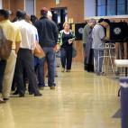 A long line of people waiting to vote, a few people standing at voting booths and a woman walking back down the line.