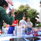 Two smiling people stand behind a table with a sign that says "Register as a voter". Two other people are coming up to the table.