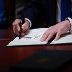 A man's hand signing a piece of paper on a desk