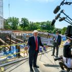 Trump standing in front of a construction site talking to a group of reporters with microphones and cameras.