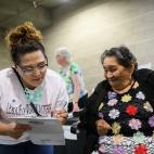 A woman lean fills out a paper on a clipboard next to another woman looking on who is holding a small American flag