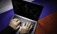 Man typing on laptop with map of United States and Russian flag in background