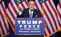 Rudy Giuliani speaking at a podium with a Trump/Pence sign on the front