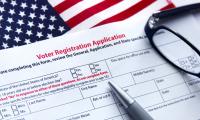 A voter registration form with a pen and glasses on top of an American flag