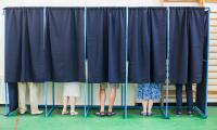 People in voting booths with only their feet visible beneath the curtains