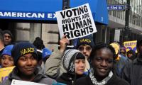 A person wearing an NAACP hat holding a voting rights sign in a crowd.