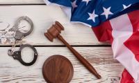 Handcuffs, a gavel and an American flag on a background of white wooden boards