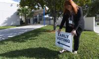 A woman sets up an 'early voting' sign on a lawn in front of a building
