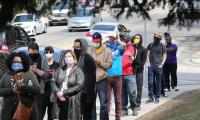 Line of people on the sidewalk wearing medical masks.