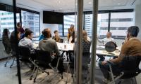 People sit around a table in a conference room seen through an open glass door