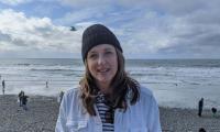 Maria Romo wearing a winter hat standing on a beach with the water behind her