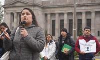 Dulce Gutierrez with a microphone, standing in front of a line of people with signs in front of a building