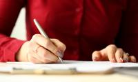 A woman in a red shirt writing on a piece of paper