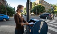A woman wearing a face mask put an absentee ballot into a mailbox on a street corner