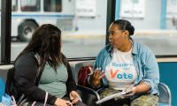 A person wearing a Restore Your Vote t-shirt talking to another person on a bench.