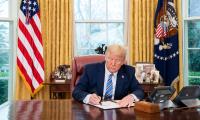 Donald Trump at his desk in the Oval Office signing a document
