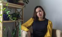 Carmelina Palmer sitting in a chair next to a bookshelf with plants on it