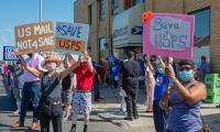 People wearing masks and holding up signs which say "Save USPS"