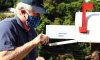 A man wearing a face mask putting an absentee ballot in the mail