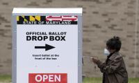 A woman puts her ballot into a large container labeled "Official Ballot Drop Box"