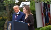 Amy Coney Barrett speaks at a podium while Donald Trump looks on