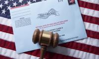 A gavel lies on top of a mail voting envelope on top of an American flag.