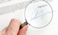 Close up of a person's hand holding a magnifying glass over a signature on a document