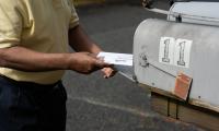 Close up of a man placing an absentee ballot into a mailbox.