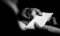 A black and white photo with one hand handing an envelope to another