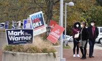 Voters wearing masks walk past signs