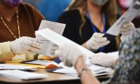 People wearing latex gloves open ballots