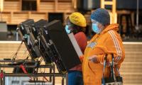 Two women wearing masks vote at electronic voting machines.