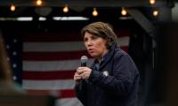 Amy McGrath speaking into a microphone while standing in front of an American Flag