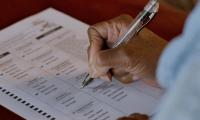 A woman's hand filling out a paper ballot with a pen.