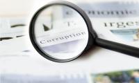 A magnifying glass held over a stack of newspapers with the word "corruption" in focus.